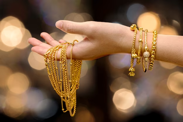 In the photo, a woman's hand is shown holding a gold bracelet and necklace jewelry. The bracelet and necklace are likely made of shiny, yellow gold, and they may feature intricate designs or embellishments.