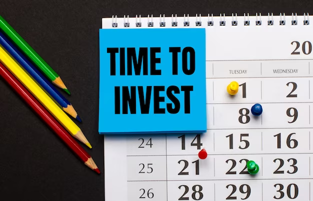 A calendar with a light blue note paper saying "Time to invest," accompanied by colored pencils on a nearby table.