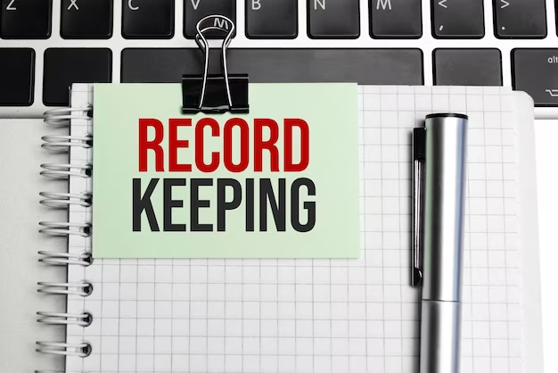 A notepad placed next to a laptop with the text "Record Keeping," symbolizing the importance of maintaining organized and accurate records for effective management and decision-making.