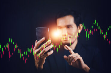 Trader using a smartphone to analyze Forex candlestick charts and copy social trading signals in real time.
