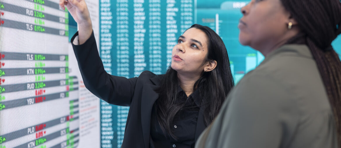 Two traders analyzing complex financial data and infographics on a large digital display screen.