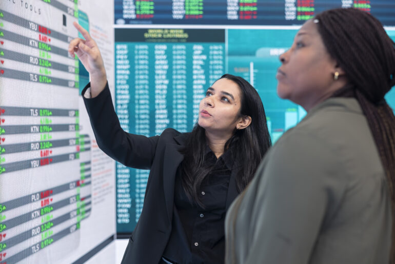 Two traders analyzing complex financial data and infographics on a large digital display screen.
