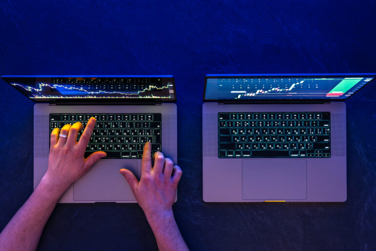 Trader analyzing stock market charts on two laptops comparing manual trading and automated trading strategies.