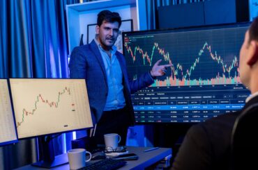 Two stock traders analyzing market charts on large screens while discussing break of structure (BOS) trading setup.