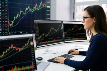 A focused female retail trader with glasses using multiple monitors displaying various live stock market charts and technical indicators.