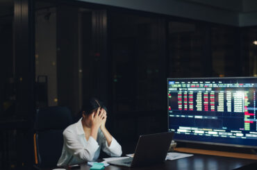 Trader analyzing stock market charts late at night while managing risk and monitoring trading drawdown on laptop screens