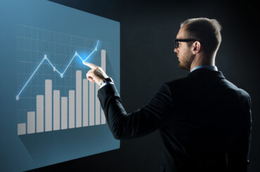 A professional trader in a suit analyzing a bullish growth chart and bar graph on a digital interface, symbolizing strategic risk management.