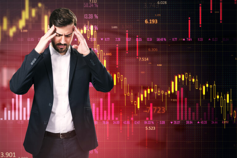 A stressed trader holding his head in front of a falling stock market candlestick chart, illustrating the failure of risk management despite having a strategy.