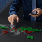 A trader pointing at a digital world map display showing green and red 3D bar charts and candlesticks representing global market volatility and geopolitical impacts on forex and commodity trading.