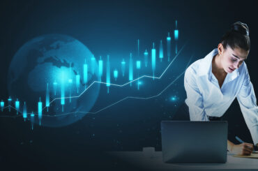 A businesswoman analyzing a glowing blue digital candlestick chart and globe hologram above a laptop, representing global financial markets, execution speed, and latency in trading infrastructure.