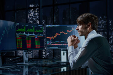 A professional trader analyzing live financial market charts and stock trends on multiple computer monitors at night, illustrating the concept of copy trading.