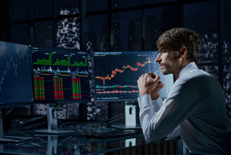 A professional trader analyzing live financial market charts and stock trends on multiple computer monitors at night, illustrating the concept of copy trading.