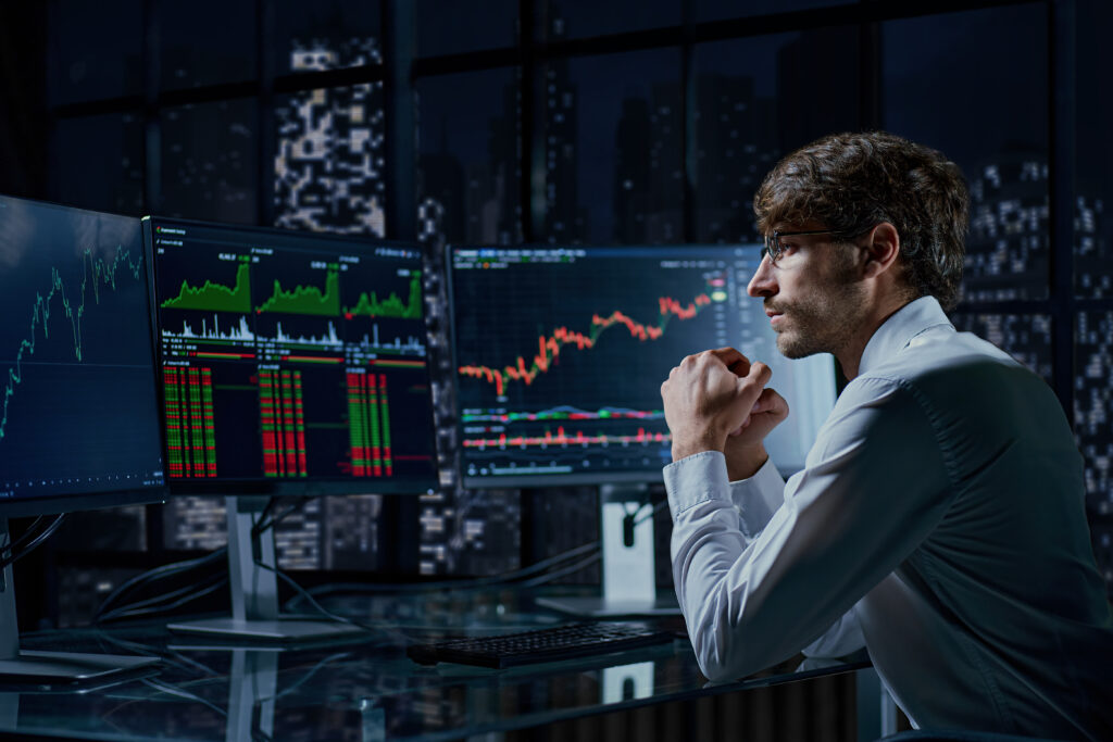 A professional trader analyzing live financial market charts and stock trends on multiple computer monitors at night, illustrating the concept of copy trading.