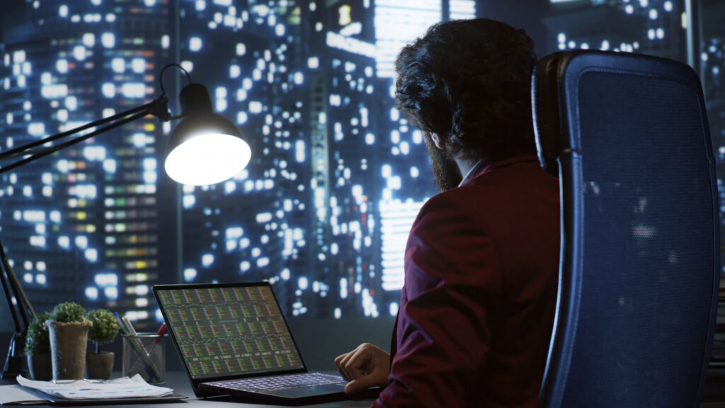 A financial analyst in a high-rise office examining crypto market charts and on-chain data metrics on a laptop at night.
