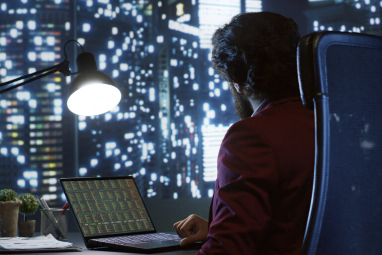 A financial analyst in a high-rise office examining crypto market charts and on-chain data metrics on a laptop at night.