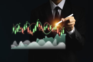 Businessman in a suit using a stylus pen to analyze financial candlestick charts and market trends for cross-asset trading